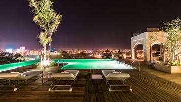 A rooftop pool area with lounge chairs and a view of the city at night.