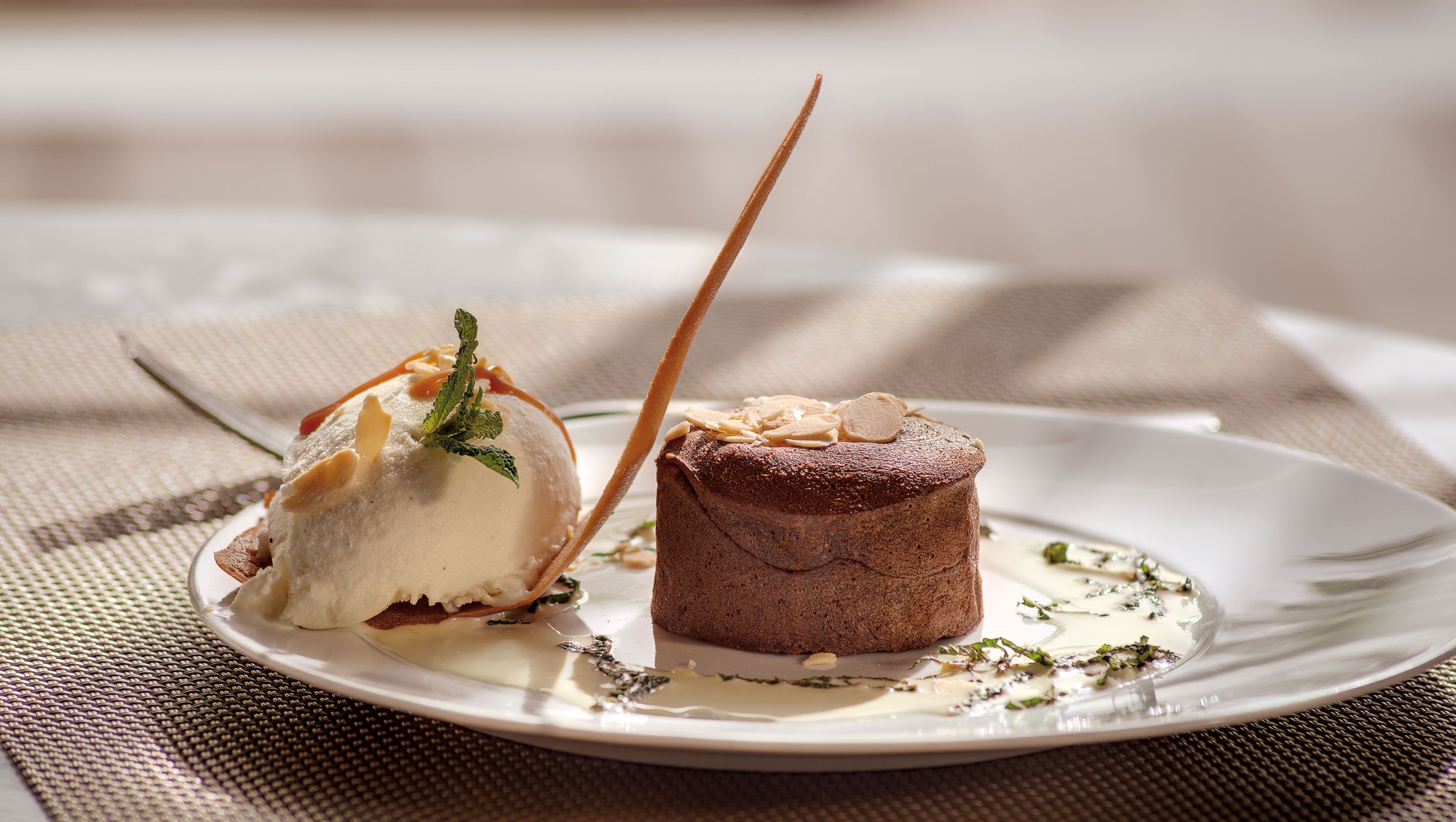 A dessert plate with a scoop of ice cream and a piece of cake, both garnished with herbs and drizzled with sauce.