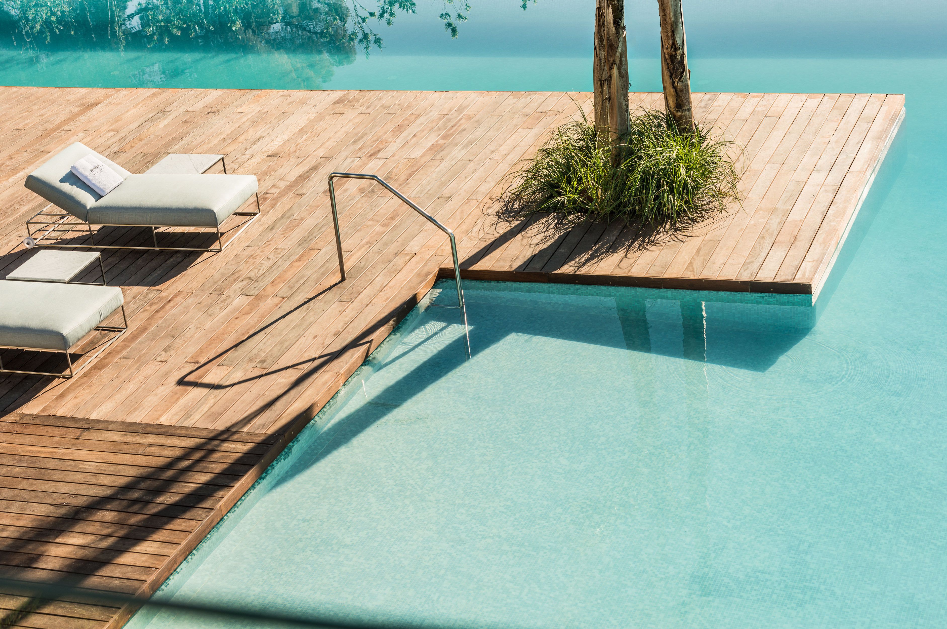 Una terraza de madera con sillones de descanso y una piscina.