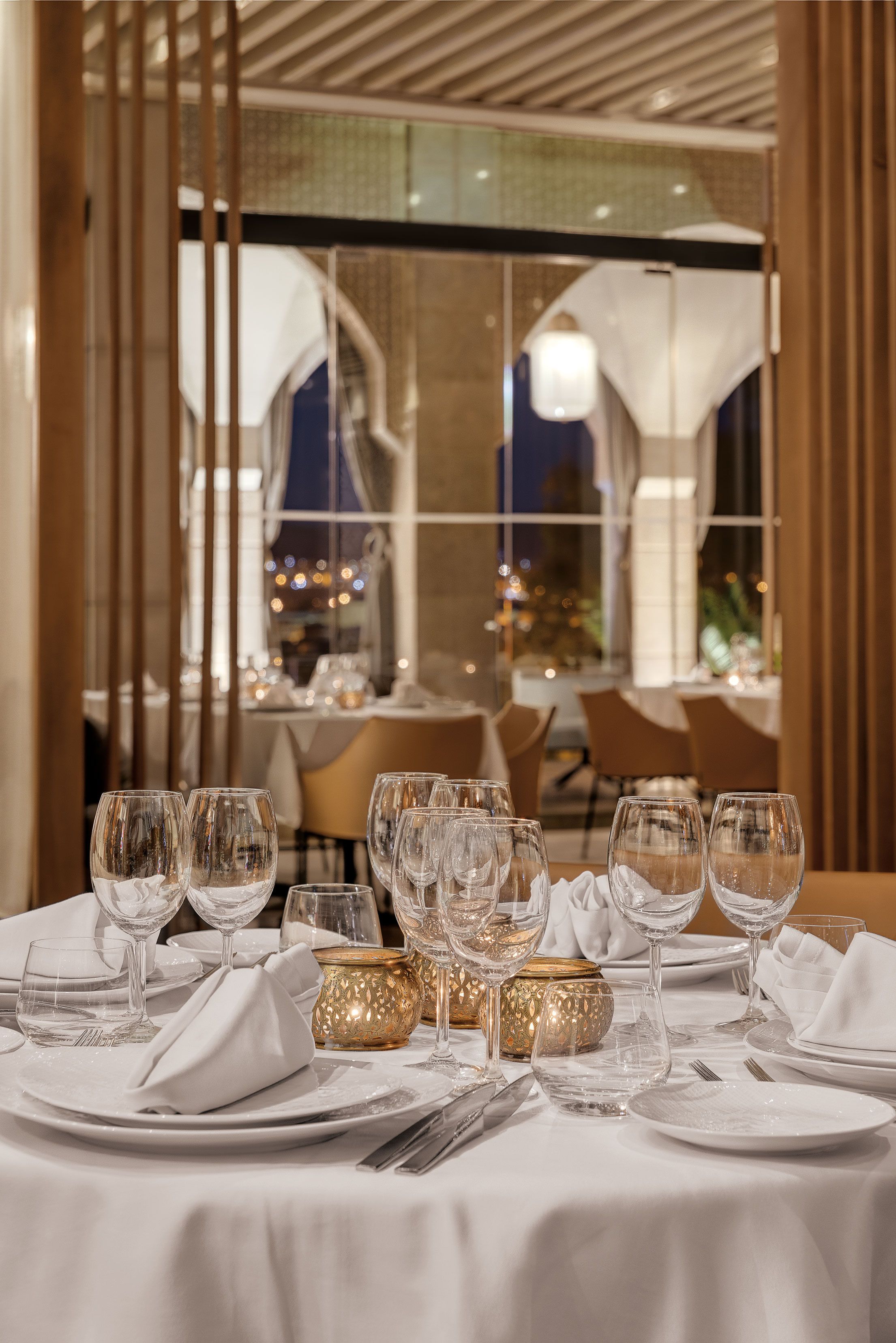 Taula de dinar posta amb diferents vasos de vi, plats i coberts, amb vista a l'interior d'un restaurant a través d'una partició de vidre.
