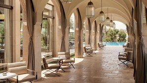 A covered outdoor seating area with cushioned chairs and tables, arched ceilings, and hanging lanterns.