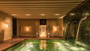 A spa area with a hot tub, wooden flooring, and a wall with a water feature.