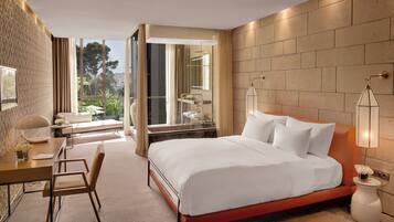 Habitación de hotel con una cama grande, un escritorio, una silla, un ventanal con vistas a zonas verdes y un baño con ducha y espejo.