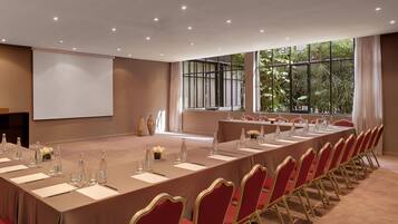 Uma sala de conferências com uma mesa comprida, cadeiras vermelhas e uma tela de projetor.