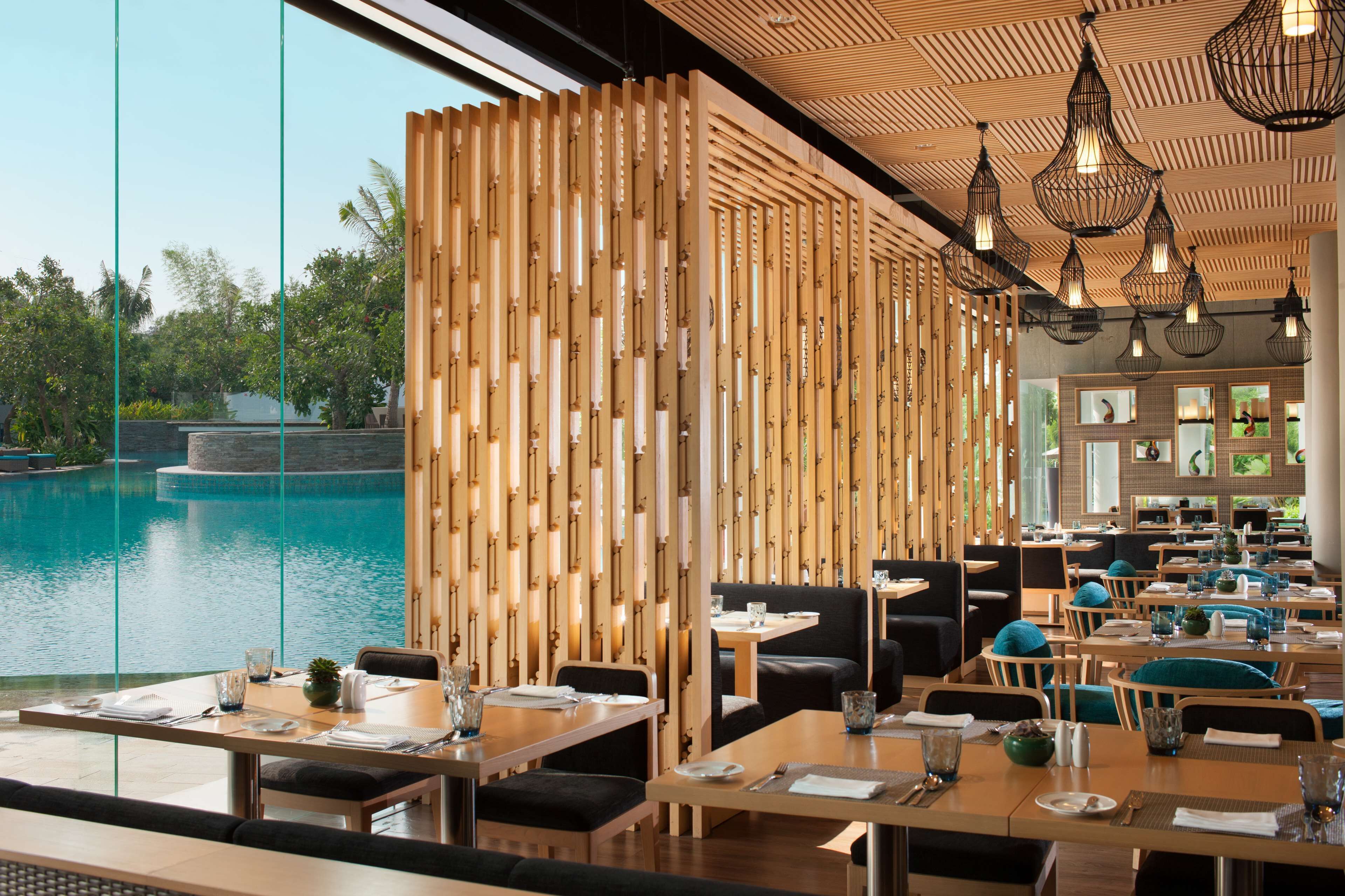 Un restaurante con vista a una piscina, separadores de madera y lámparas colgantes.