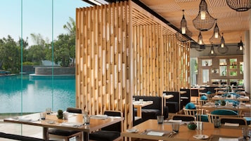 A restaurant with a view of a pool, wooden partitions, and hanging light fixtures.