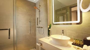 A modern bathroom with a glass shower enclosure, a white sink with a large basin, and a mirror with a circular frame.