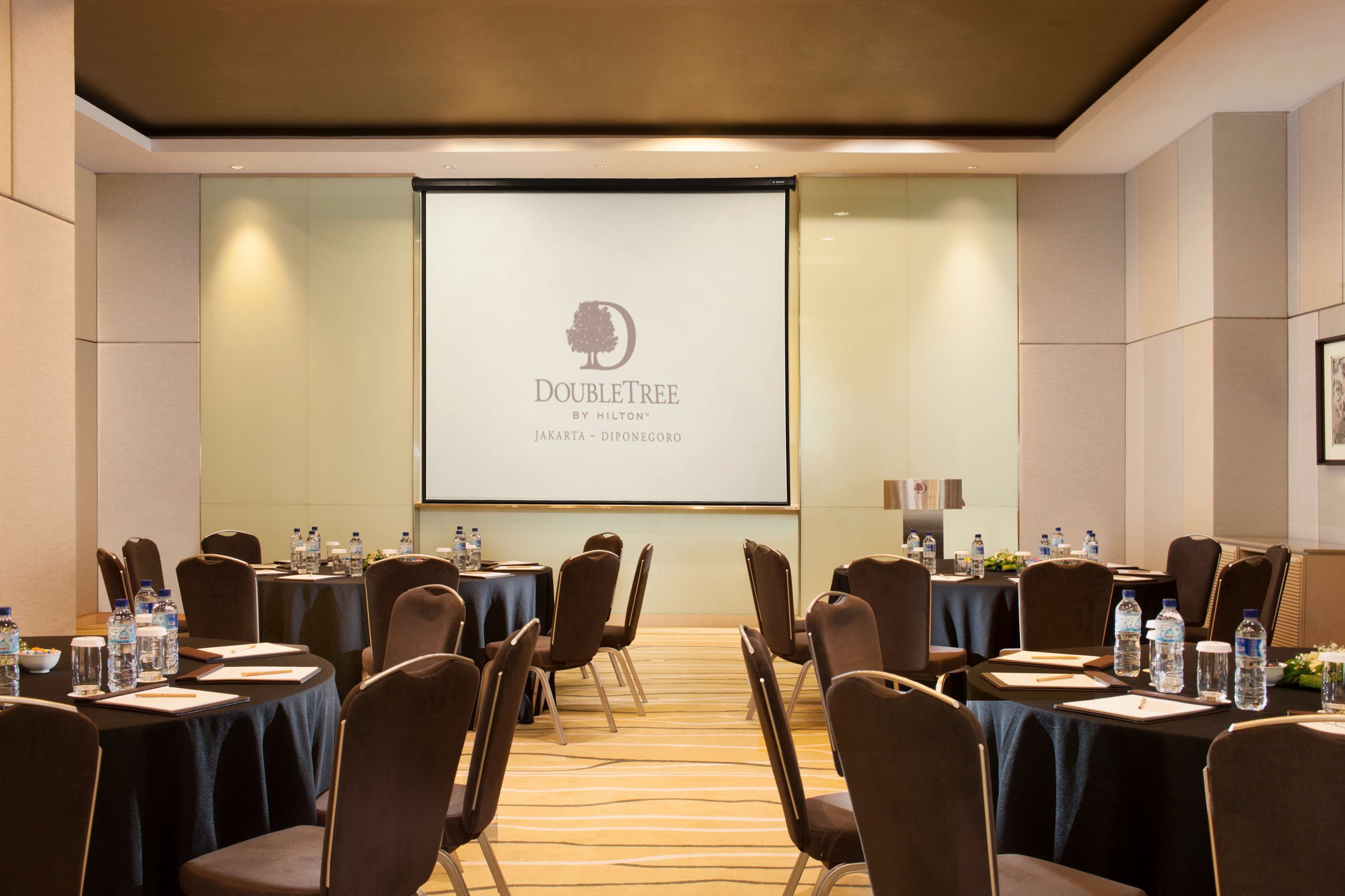 A conference room with tables, chairs, and a projector screen displaying the DoubleTree logo.