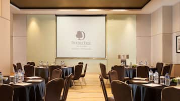 Uma sala de conferências com mesas, cadeiras e uma tela de projeção exibindo o logotipo da DoubleTree.