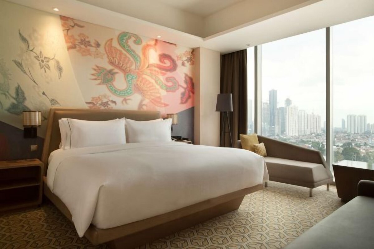 A hotel room with a large bed, a sofa, a city view, and a decorative wall mural.