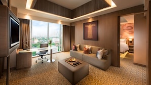 Una habitación de hotel moderna con una cama grande, un sofá, un escritorio con televisor y vistas a la ciudad.