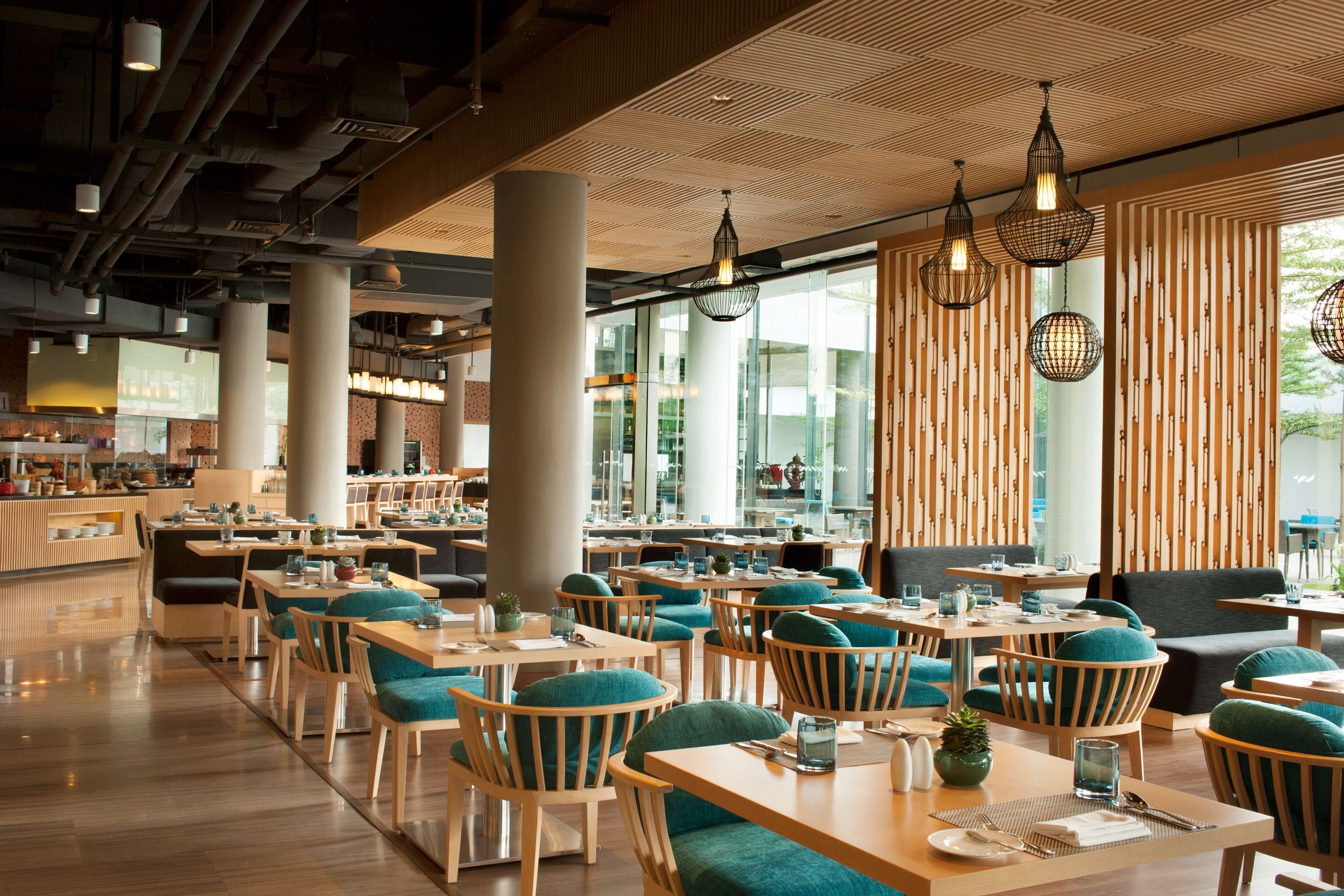 A modern restaurant with wooden tables and chairs, large windows, and hanging pendant lights.
