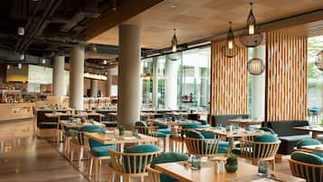 A modern restaurant with wooden tables and chairs, large windows, and hanging pendant lights.