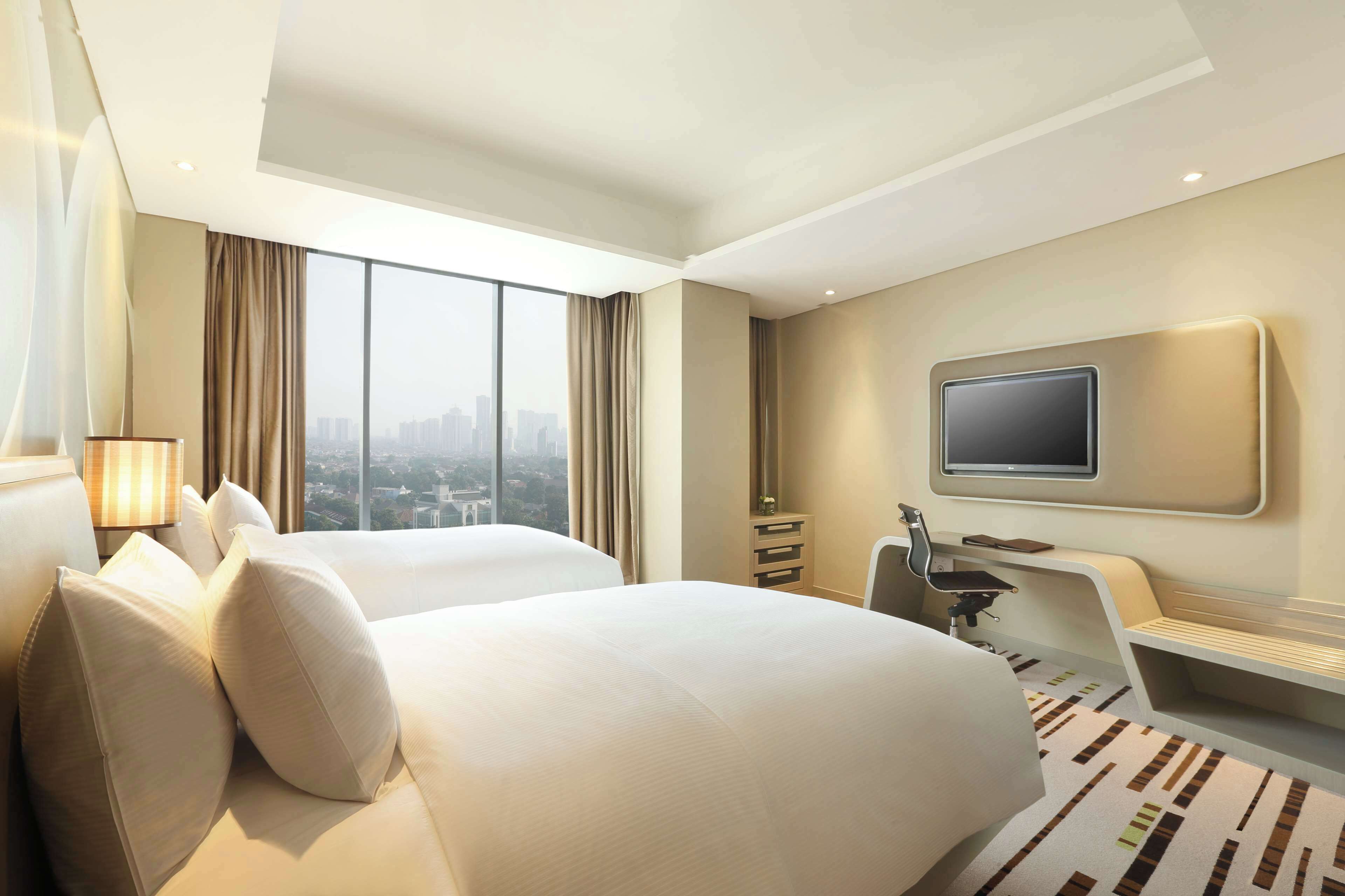 Habitación de hotel con dos camas, un escritorio, una silla, un televisor y vistas a la ciudad.