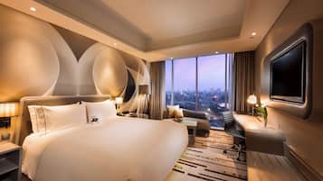 A modern hotel room with a large bed, a desk, a chair, and a TV.