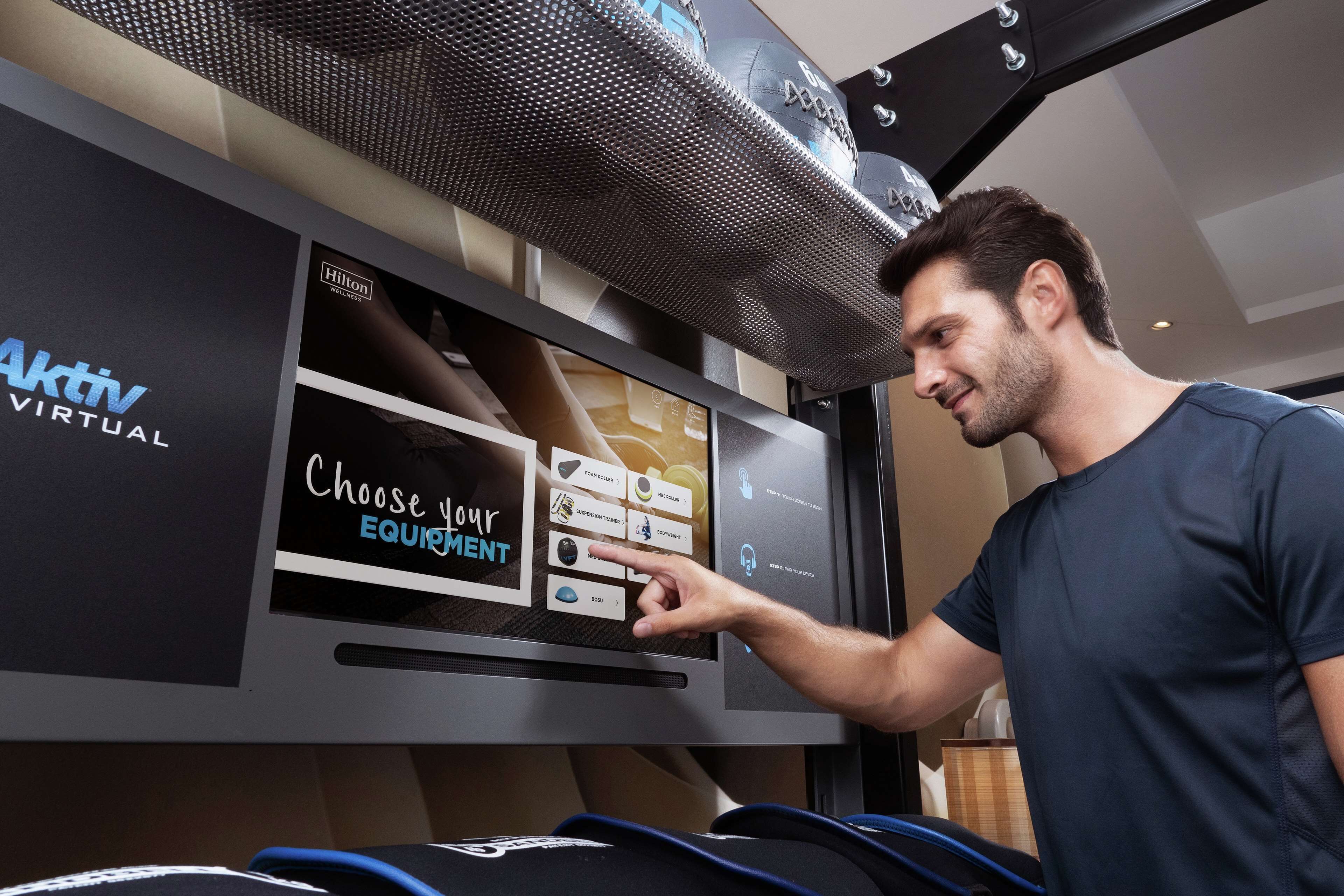 Un hombre interactuando con un quiosco digital en un hotel, mostrando opciones para equipamiento y servicios de la habitación.