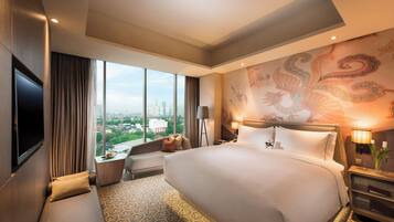 A hotel room with a large bed, a sofa, a TV, a desk, and a view of the cityscape.
