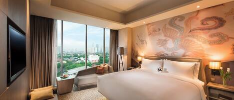 A hotel room with a large bed, a sofa, a TV, a desk, and a view of the cityscape.