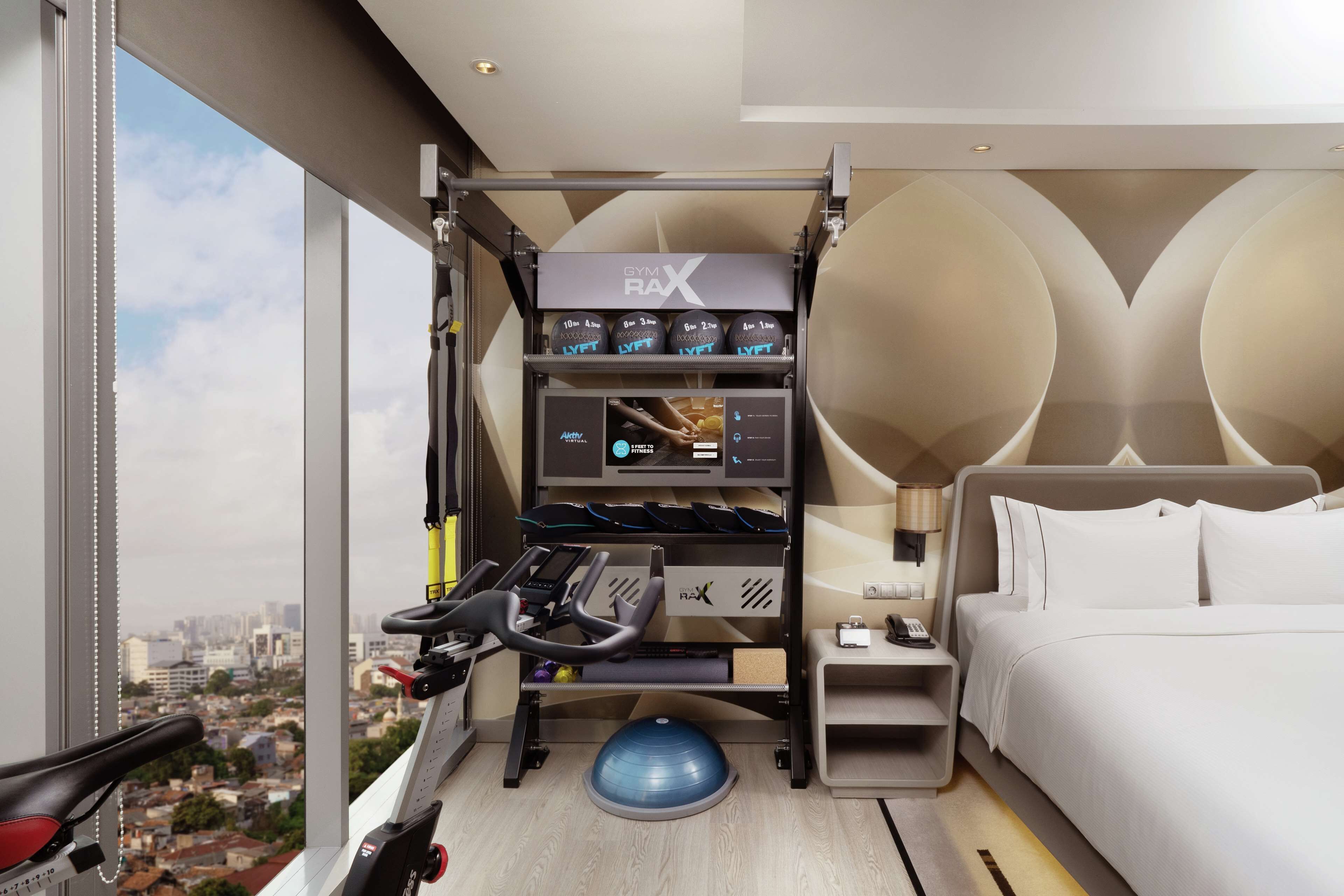 A hotel room with a gym area, including a treadmill, exercise balls, and a wall-mounted rack with gym equipment.