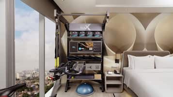 A hotel room with a gym area, including a treadmill, exercise balls, and a wall-mounted rack with gym equipment.