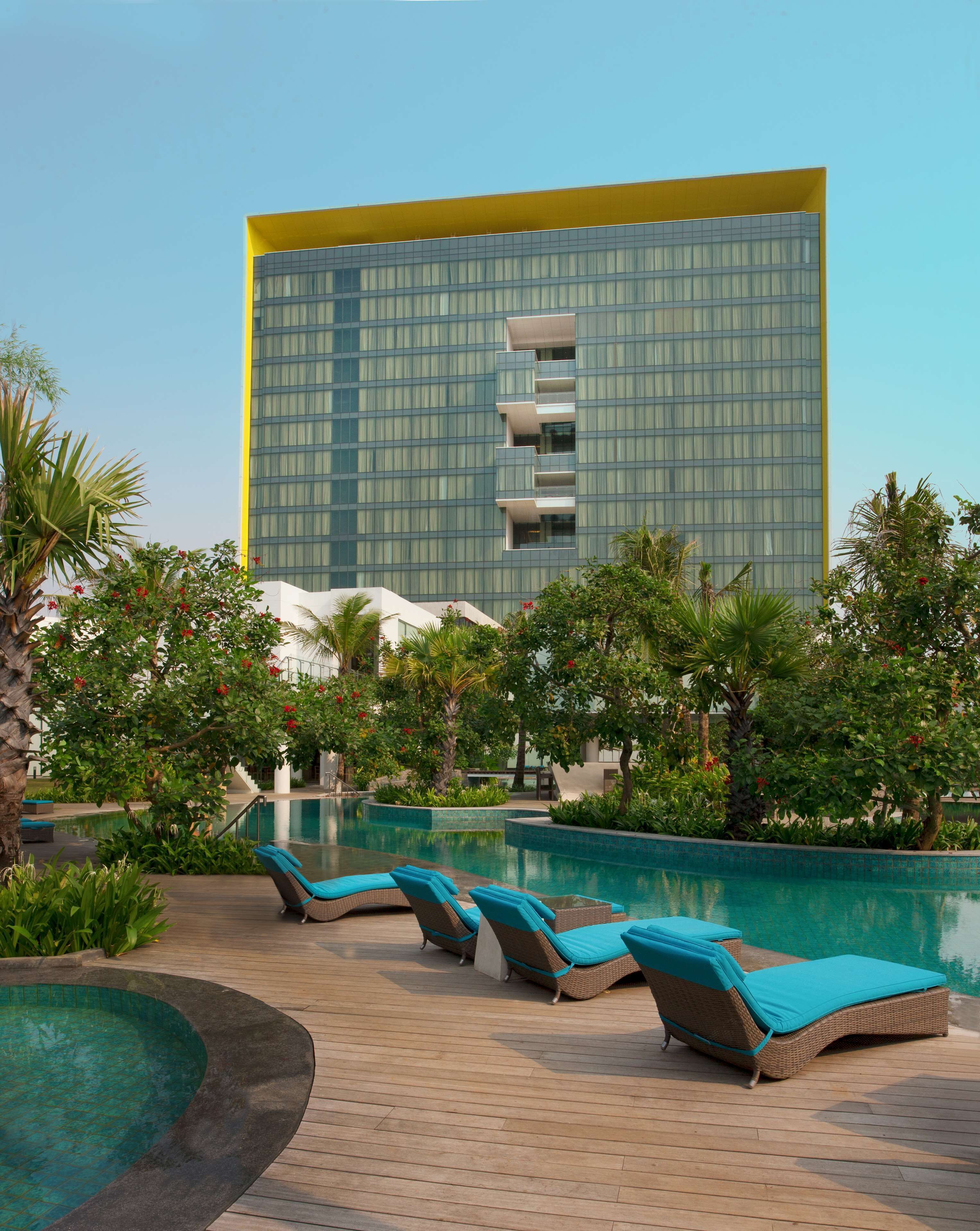 Een modern hotel met een groot glazen gebouw, een zwembad en lounge stoelen.