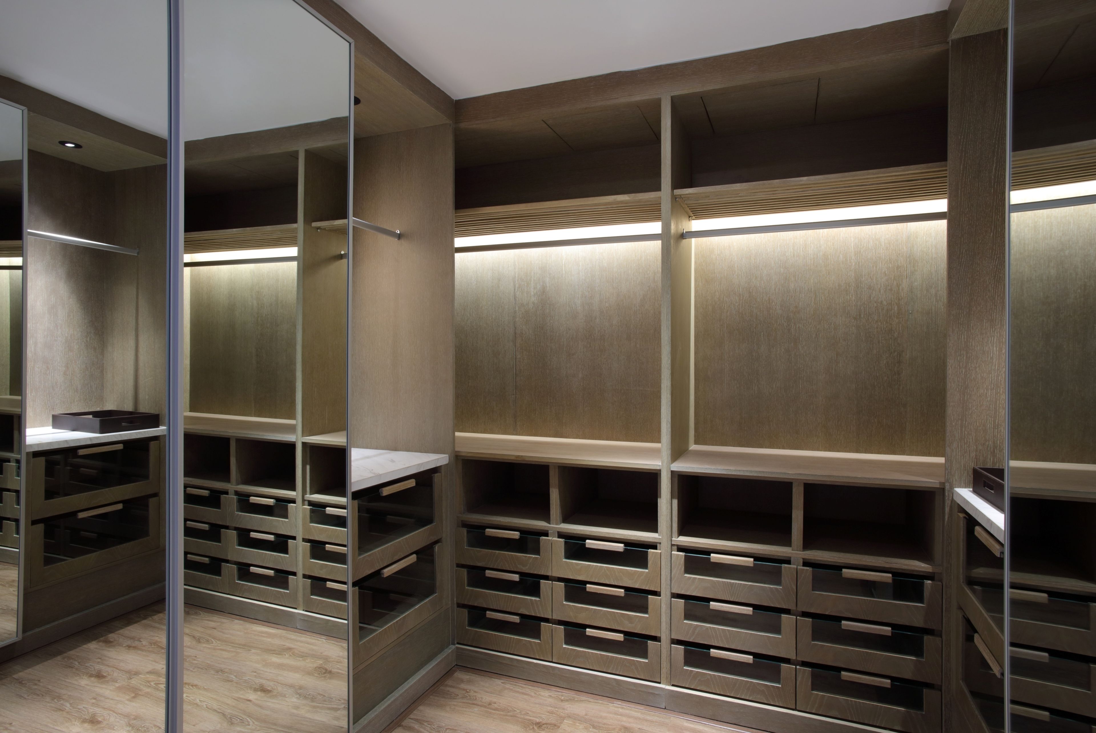 A walk-in closet with mirrored doors, wooden shelving, and integrated lighting.