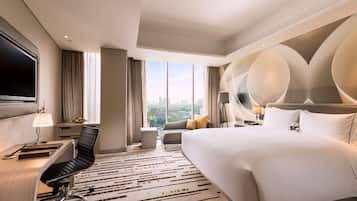 Una habitación de hotel moderna con una cama grande, un escritorio con silla, un televisor de pantalla plana y vistas a la ciudad.