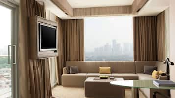 Una habitación de hotel moderna con un ventanal grande, un sofá, una mesa de centro y un televisor montado en la pared.