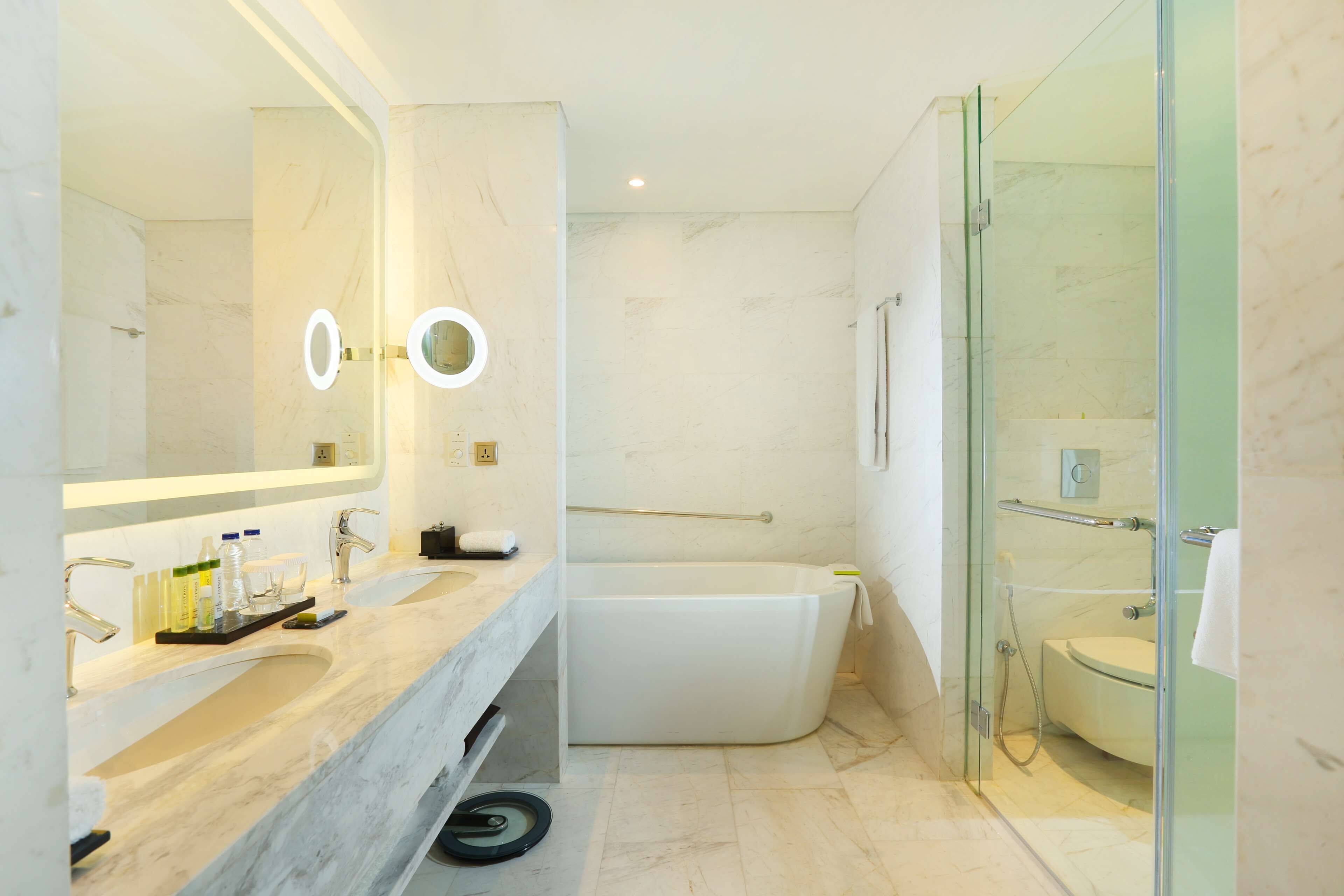Un baño moderno con un espejo grande, dos lavamanos, una bañera y zona de ducha con mampara de vidrio.