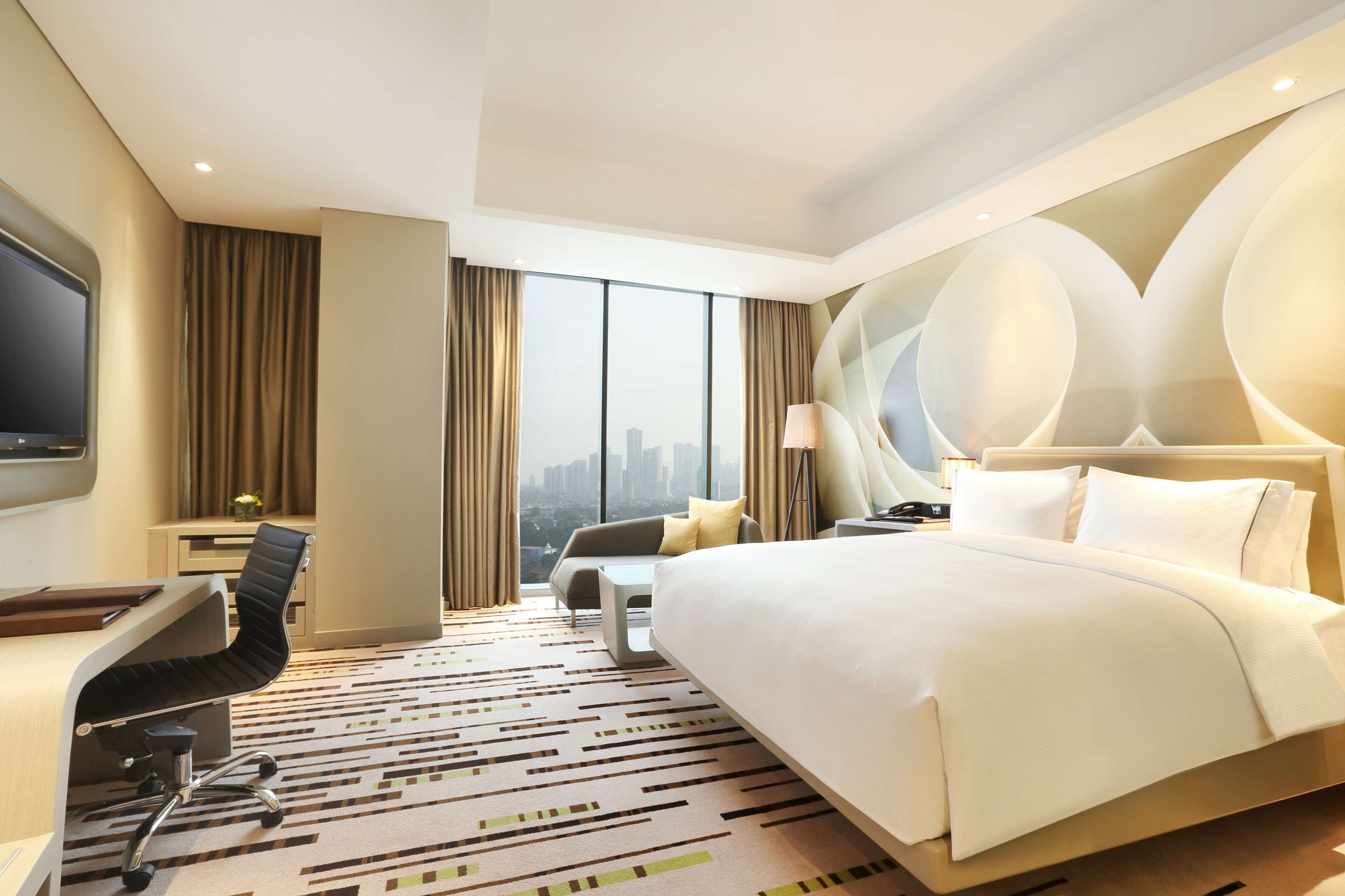 Habitación de hotel con una cama grande, un escritorio con una silla, un televisor y vistas a la ciudad.