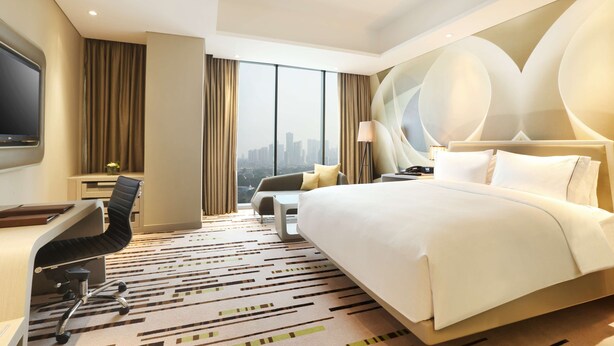 A hotel room with a large bed, a desk with a chair, a TV, and a view of the city. - DoubleTree by Hilton Jakarta - Diponegoro (Jakarta)