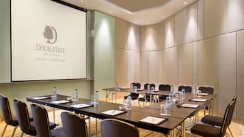 Un salón de conferencias con una larga mesa, sillas y una pantalla proyectora mostrando el logotipo de DoubleTree Jakarta.