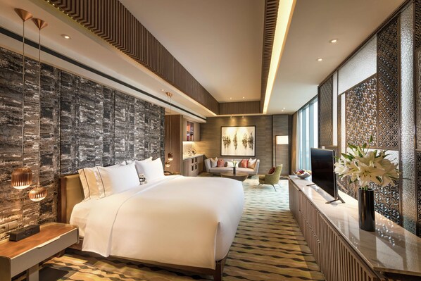 A modern hotel room with a large bed, a seating area with a sofa and armchairs, a desk with a computer, and a decorative vase with flowers. - DoubleTree by Hilton Jakarta - Diponegoro (Jakarta)