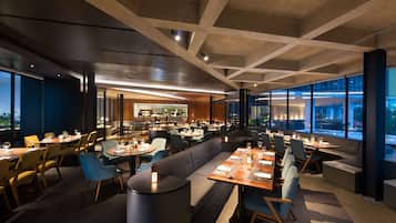 Un restaurante moderno con diversas opciones de asientos, incluyendo mesas, cabinas y una zona de bar.