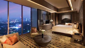Una habitación de hotel moderna con una cama grande, un sofá, una mesita de café y un televisor. La habitación tiene vista a la ciudad y un ventanal amplio.