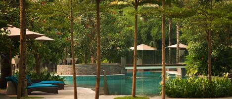 A poolside area with lounge chairs, a pool, and surrounding greenery.