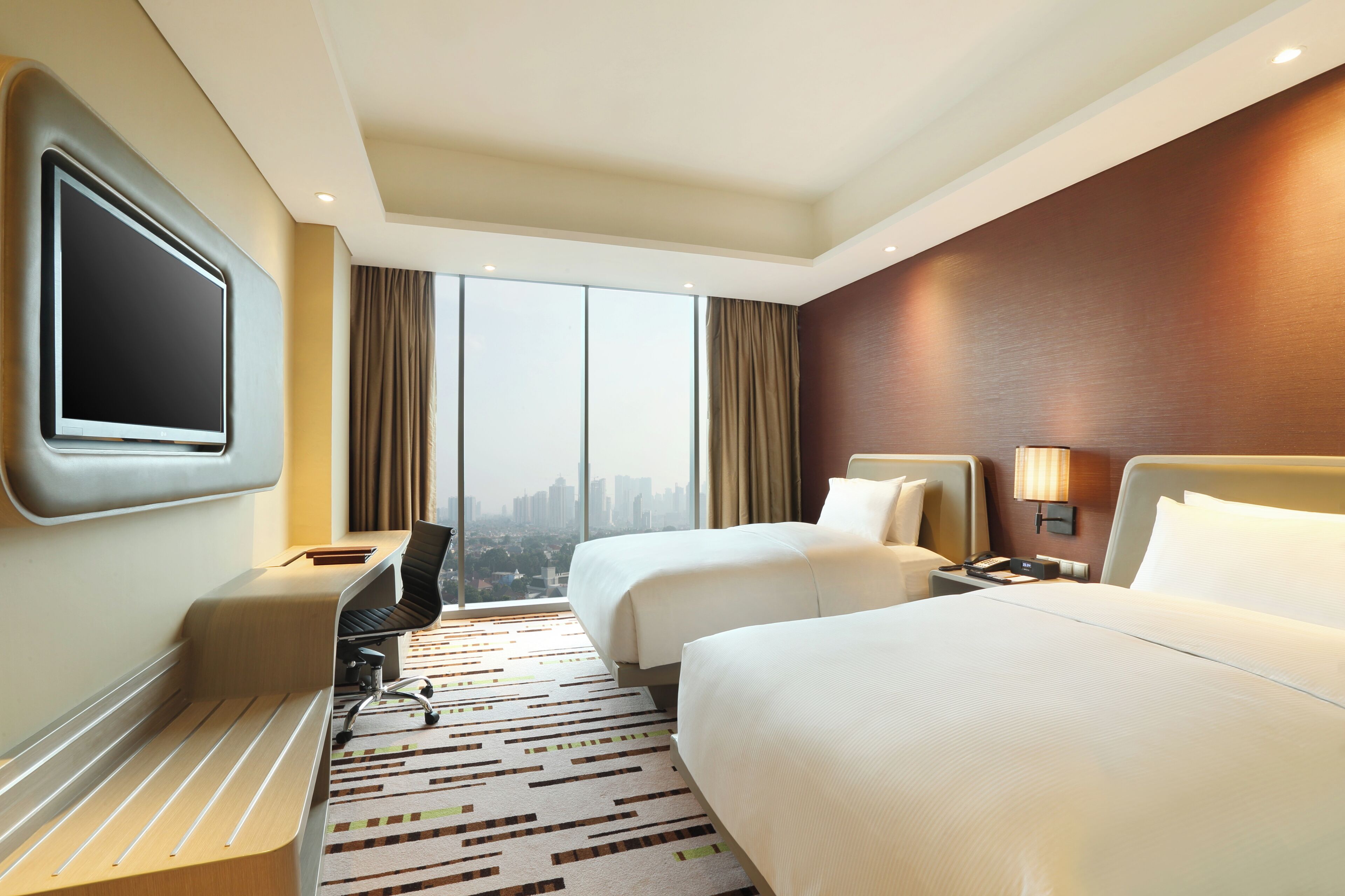 A hotel room with a large TV, two beds, a desk, and a view of the city.