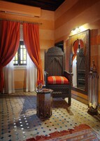 Una habitación tradicional con piso estampado, un sillón grande y decorado con un cojín rojo, y un espejo con detalles intrincados.