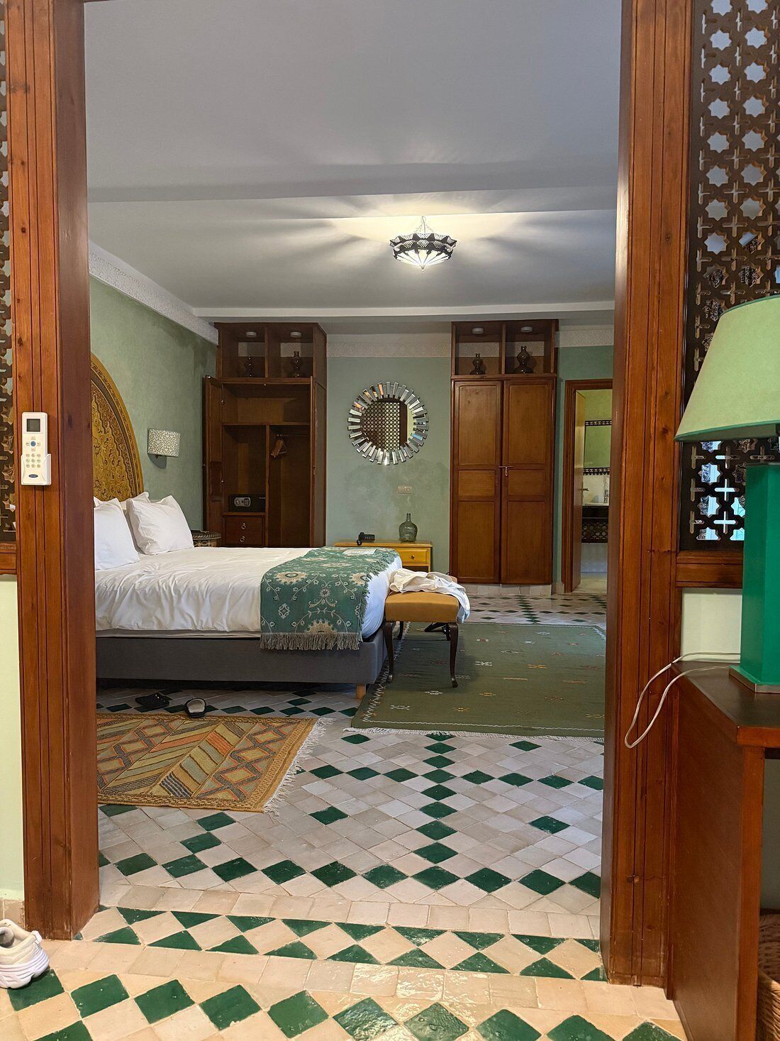 Un dormitorio con cama, mesita de noche, lámpara, espejo y suelo estampado.