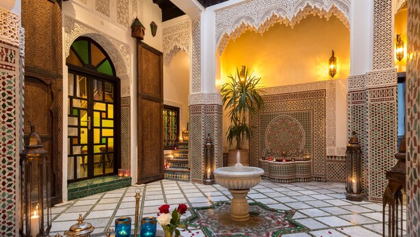 A traditional Moroccan interior with intricate tile work, a fountain, and a tea set on a tray. - Algilà Fes Riad Medina Charme Hotel Spa (Fes)
