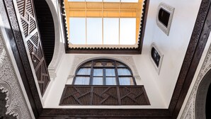 A view from a balcony with intricate white and dark wood carvings, a large arched window, and a patterned ceiling. - Algilà Fes Riad Medina Charme Hotel Spa (Fes)
