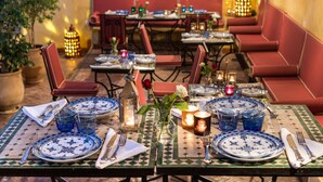 An outdoor dining area with tables set for two, featuring blue and white patterned plates, silverware, and candles. - Algilà Fes Riad Medina Charme Hotel Spa (Fes)