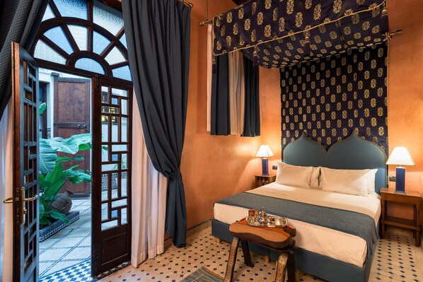 Un dormitorio con cama con dosel, una mesita de noche con lámpara y vistas a un espacio exterior con plantas a través de una puerta.