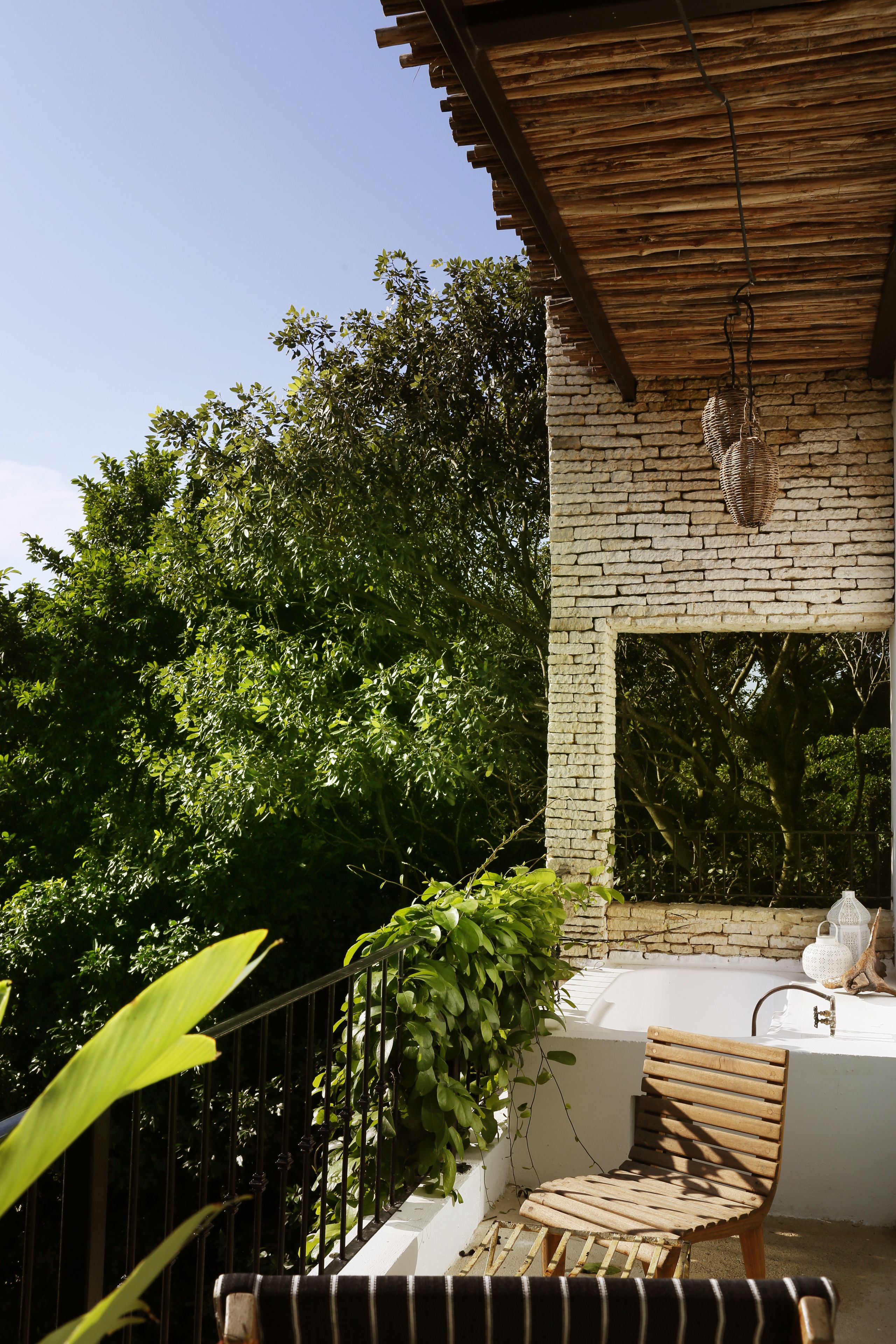 A wooden bench and a white bathtub under a wooden pergola, surrounded by lush greenery.