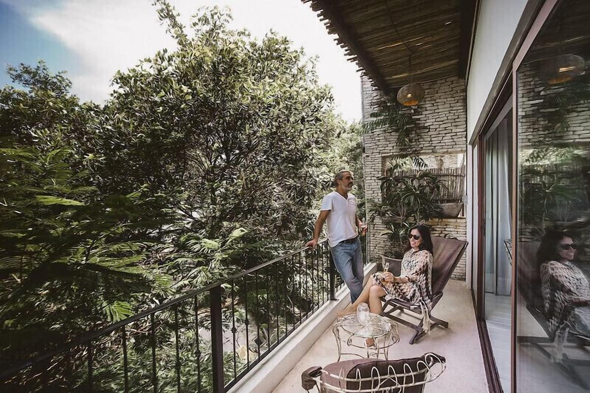 A balcony with a glass railing, a stone wall, and a view of dense foliage.