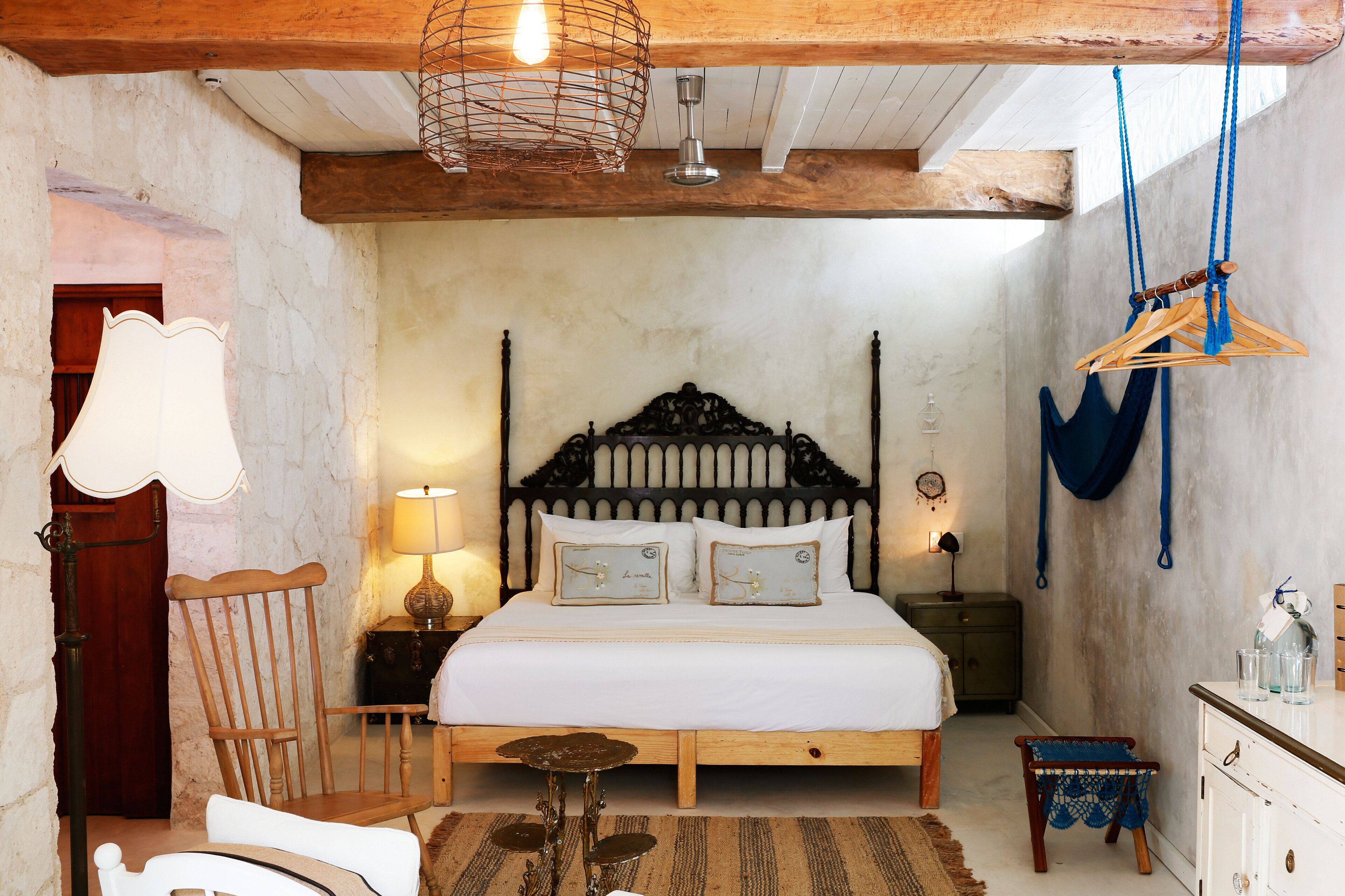Un dormitorio con una cama de madera, una silla, una mesita y una lámpara colgante.