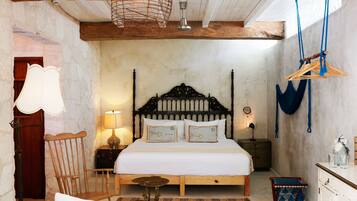 Un dormitorio con una cama de madera, una silla, una mesita y una lámpara colgante.