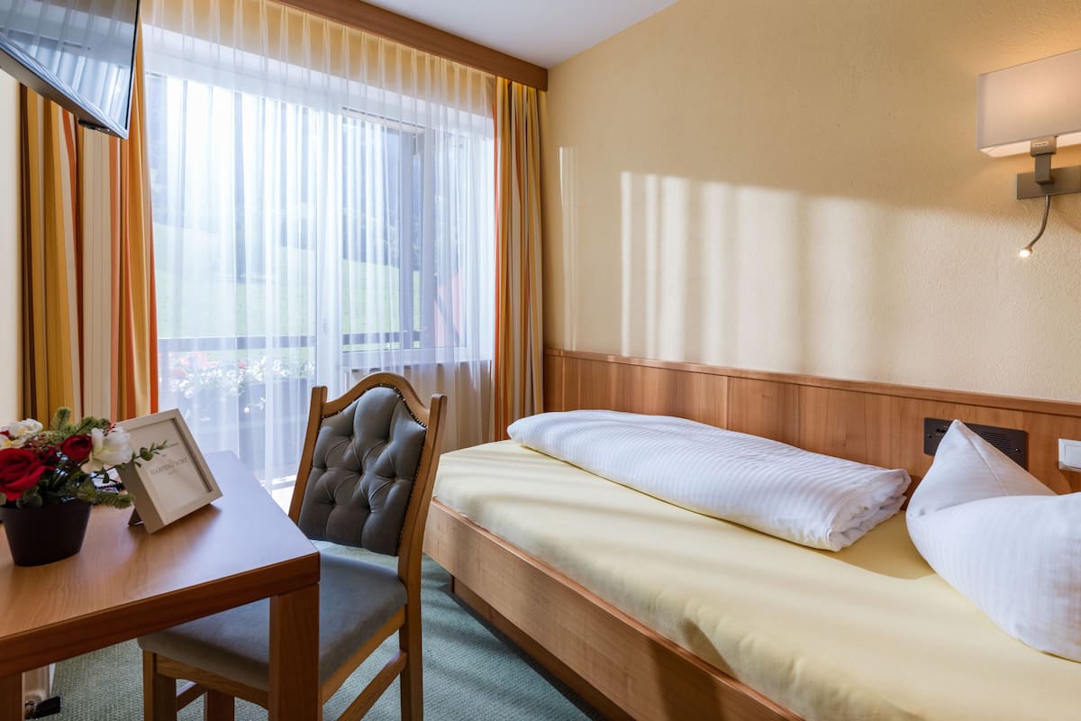 Une chambre d’hôtel avec un lit, un bureau, une chaise, un tableau encadré et une fenêtre avec des rideaux.
