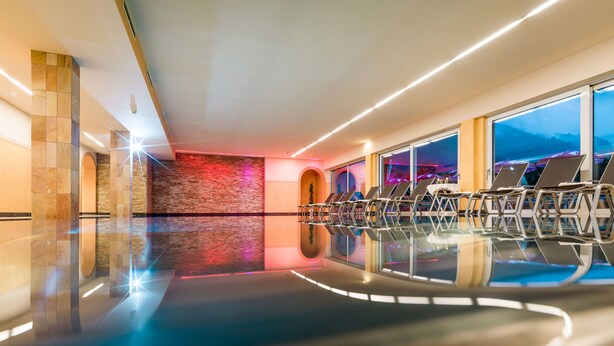 Een modern binnenzwembad met helder water, ligbedden en uitzicht op de bergen door grote ramen.