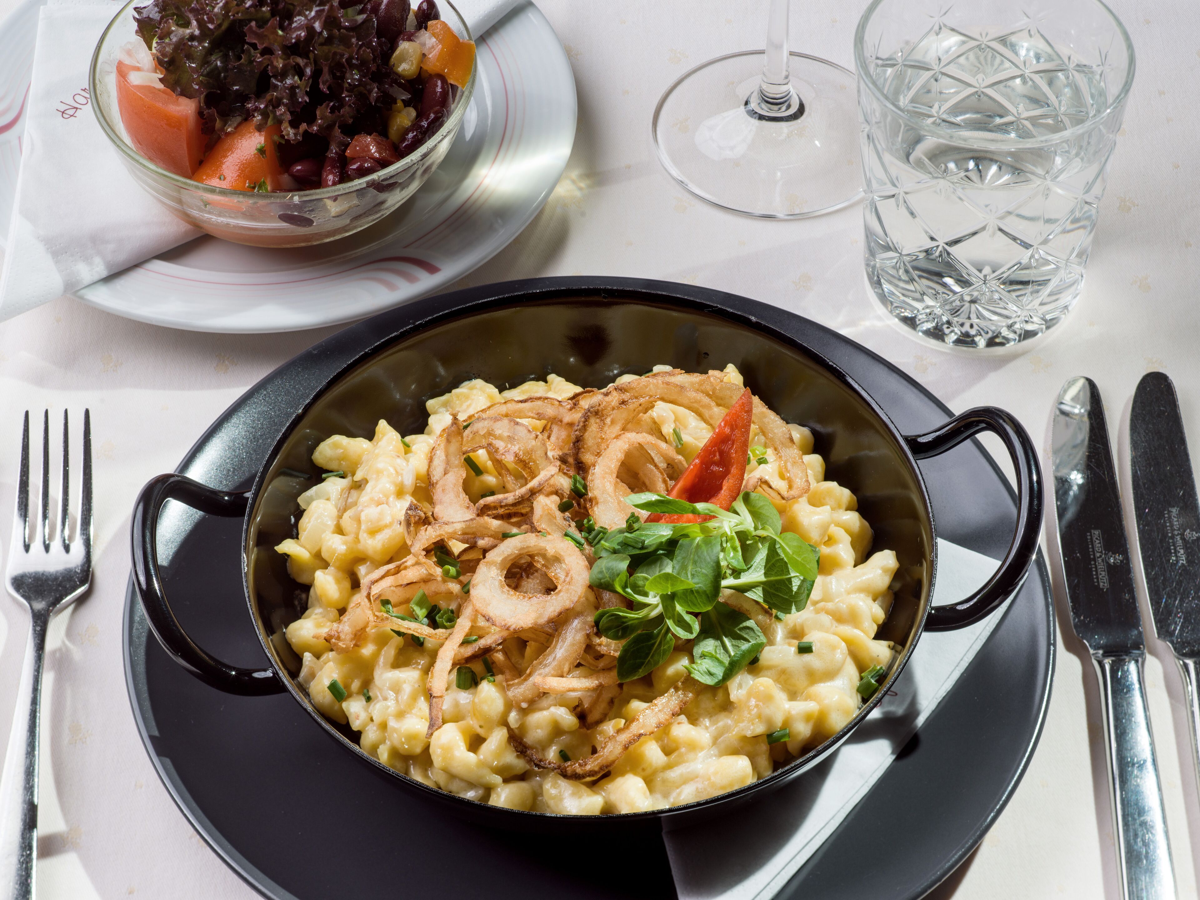 A meal with macaroni and cheese, onions, and greens, served in a black skillet on a white plate.